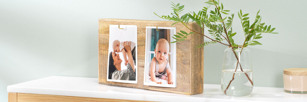 Due foto di bambini in una cornice su un ripiano di legno accanto a una pianta.