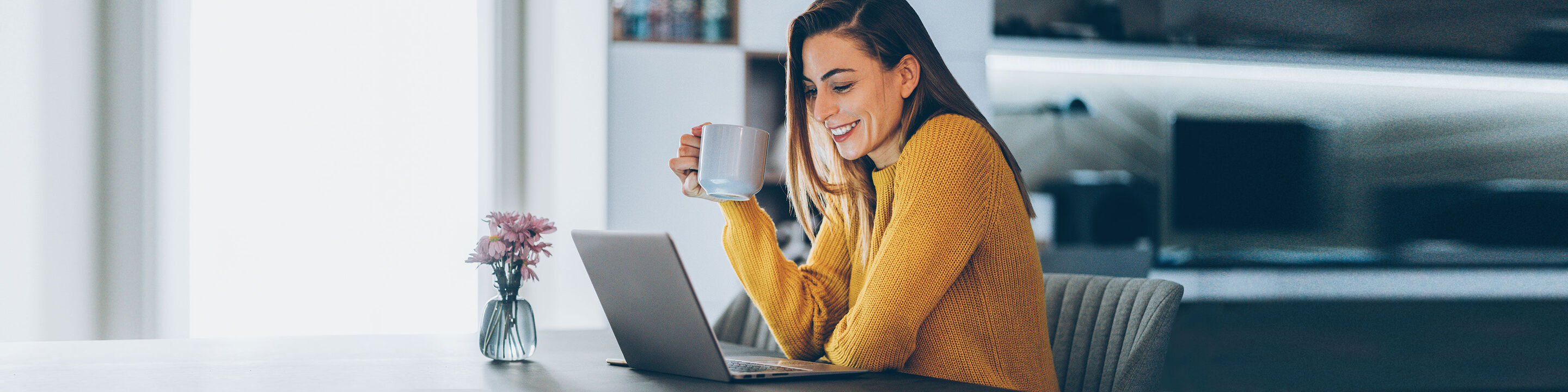 Una persona in maglione giallo si gode una tazza di caffè mentre lavora al laptop