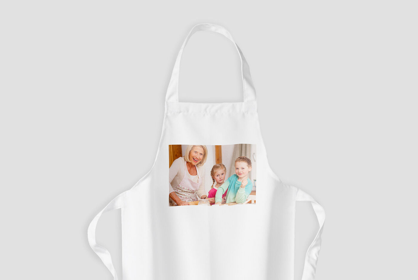 Un grembiule bianco con un'immagine di due bambini sorridenti. Il grembiule simboleggia momenti di cucina creativa.