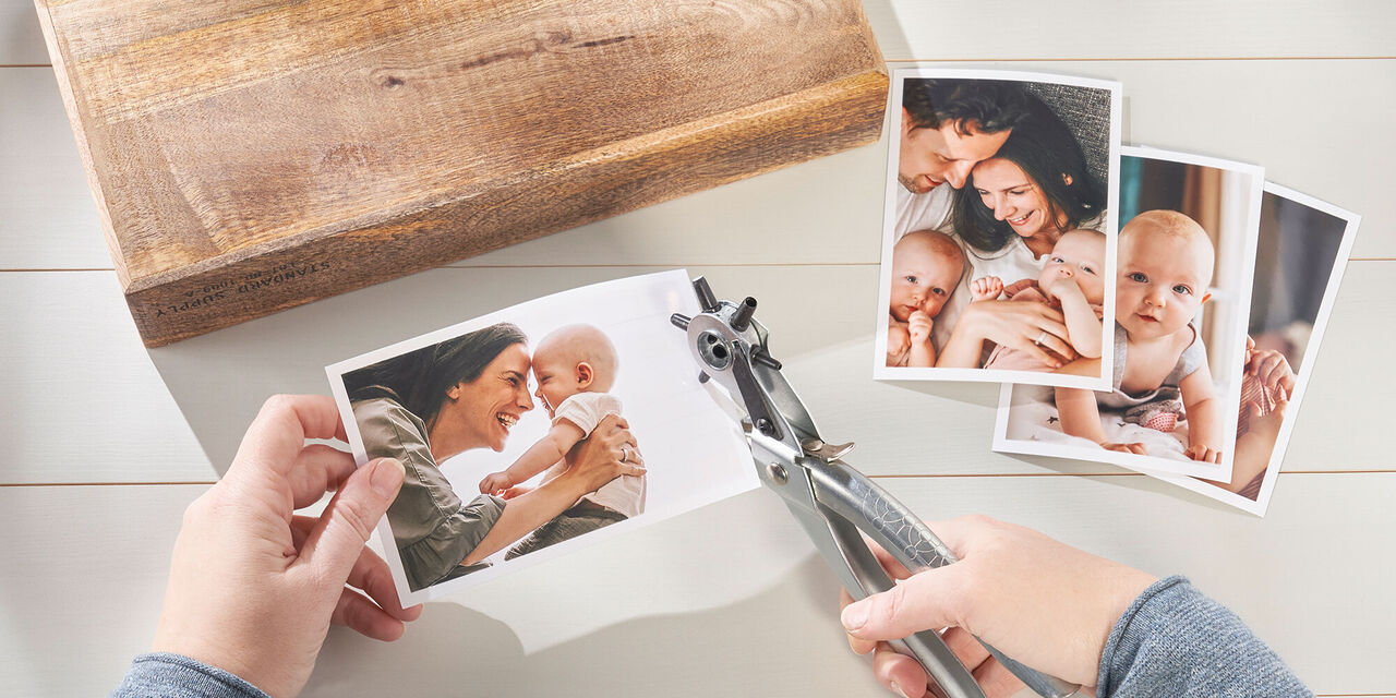 Una persona ritaglia foto con cura, sul tavolo ci sono diverse foto e un legno.