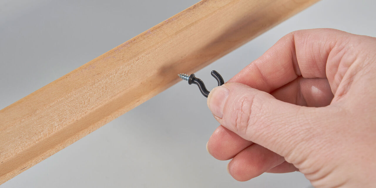 Una mano tiene un gancio nero con vite, pronta per essere inserita in un tavoletta di legno