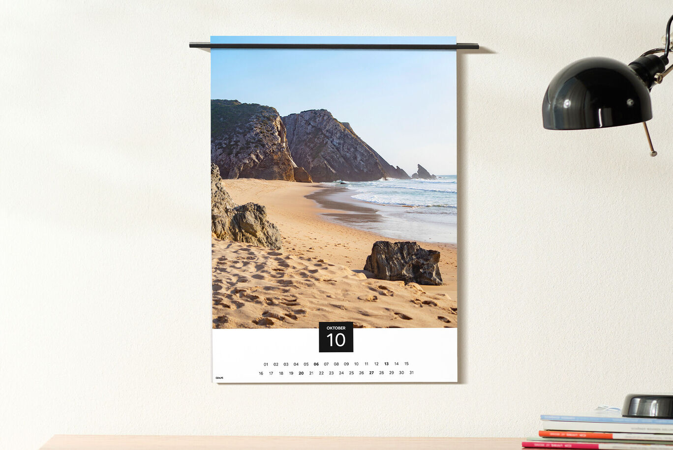 Un calendario da parete con una bella immagine di spiaggia. La costa presenta onde dolci e sabbia dorata in una giornata di sole.
