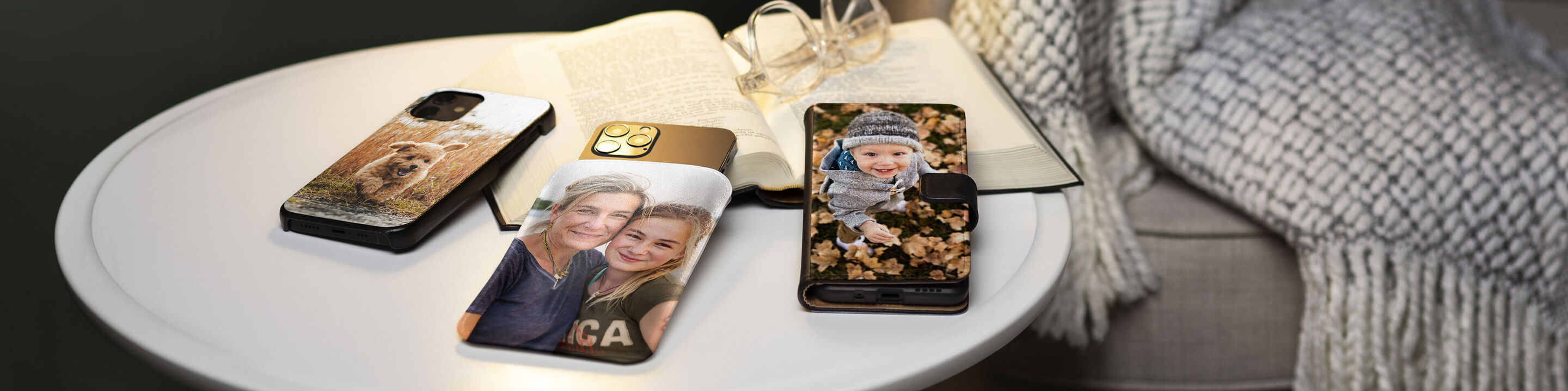 Tre telefoni con custodie personalizzate su un tavolo. Due mostrano foto di persone, il terzo ha un design floreale.