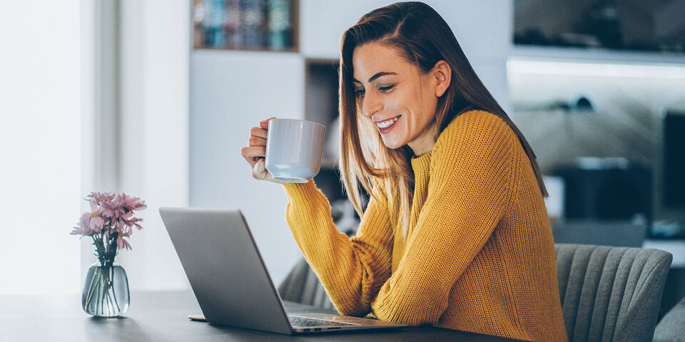 Una persona con una tazza di caffè lavora al computer portatile a un tavolo