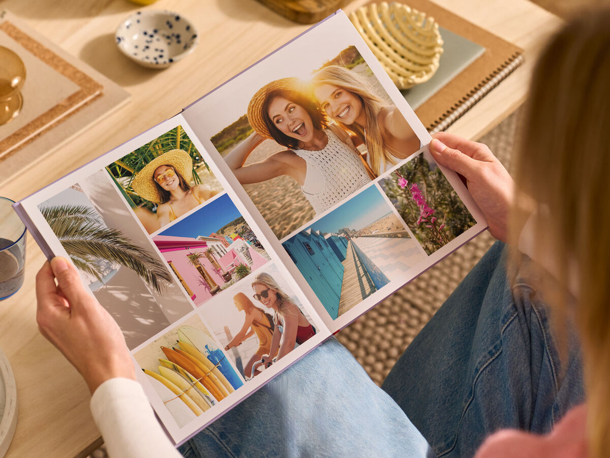 Una donna è seduta su un divano in salotto, con in mano un FOTOLIBRO CEWE aperto.