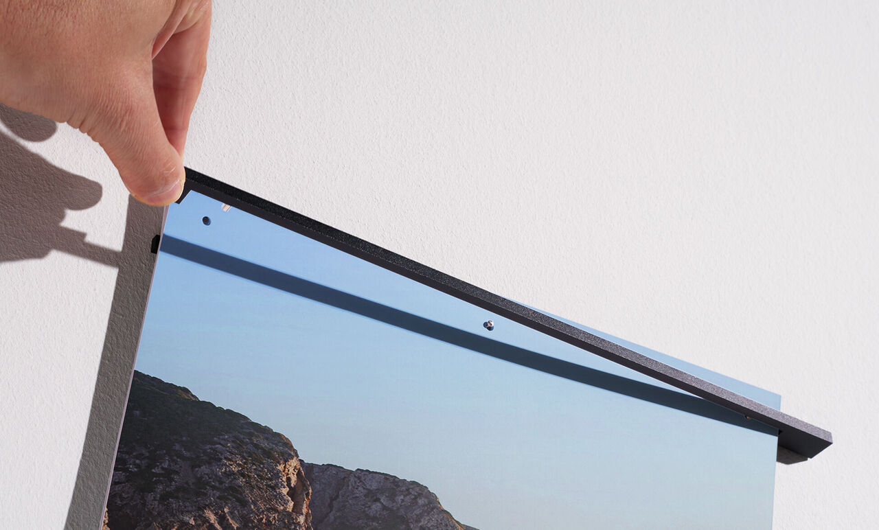 Una persona appende un quadro CEWE al muro. Il quadro mostra un paesaggio.