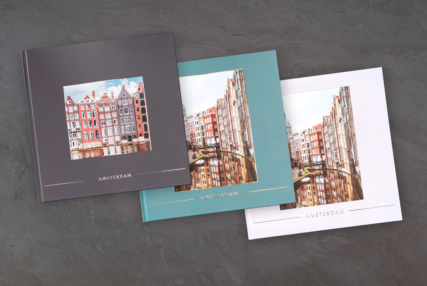Tre diversi fotolibri CEWE con immagini di Amsterdam, ciascuno con uno schema di colori diverso.