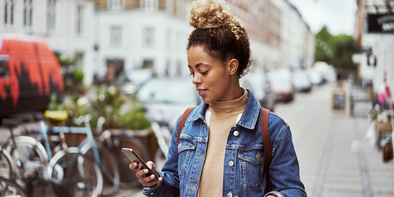 Giovane donna in città con uno smartphone in mano, sorride e si gode il momento.