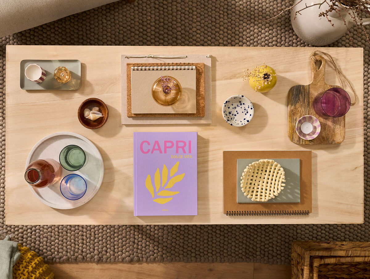 Un FOTOLIBRO Cewe è appoggiato su un tavolino da caffè. La copertina è rosa e riporta la parola "Capri".