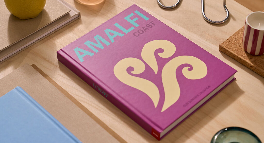 Un fotolibro CEWE è su un tavolo. La copertina è viola e riporta la parola "Amalfi".