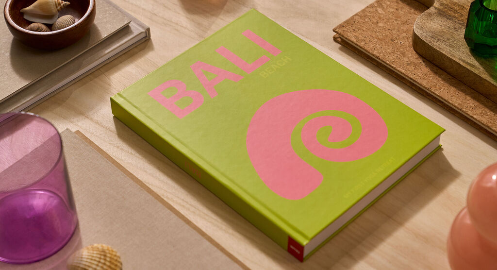 Un fotolibro CEWE è poggiato su un tavolo. La copertina è verde chiaro e riporta la parola "Bali".