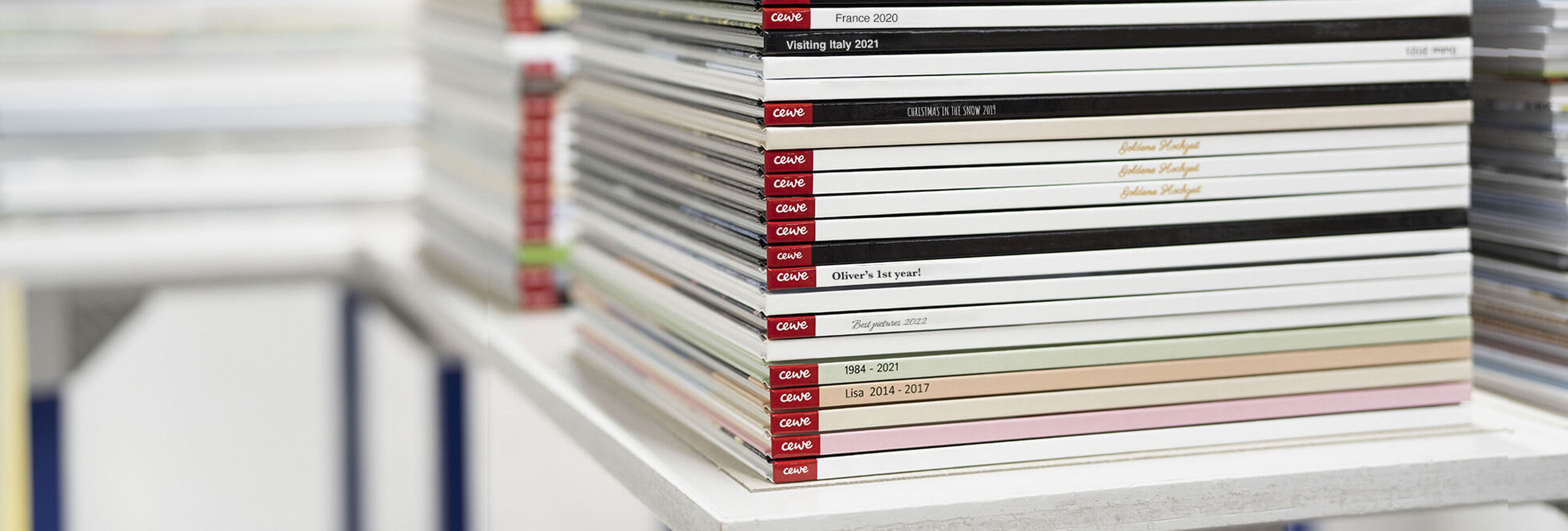 Colorati fotolibri CEWE impilati su uno scaffale bianco
