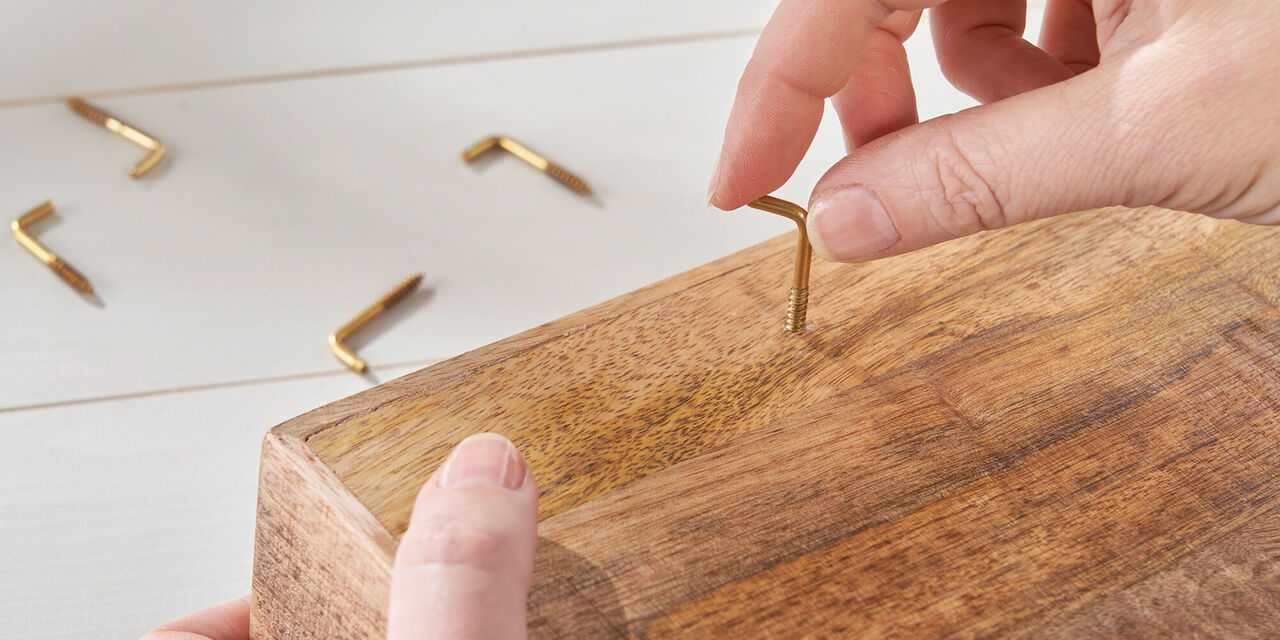 Una persona inserisce una vite dorata in un legno.