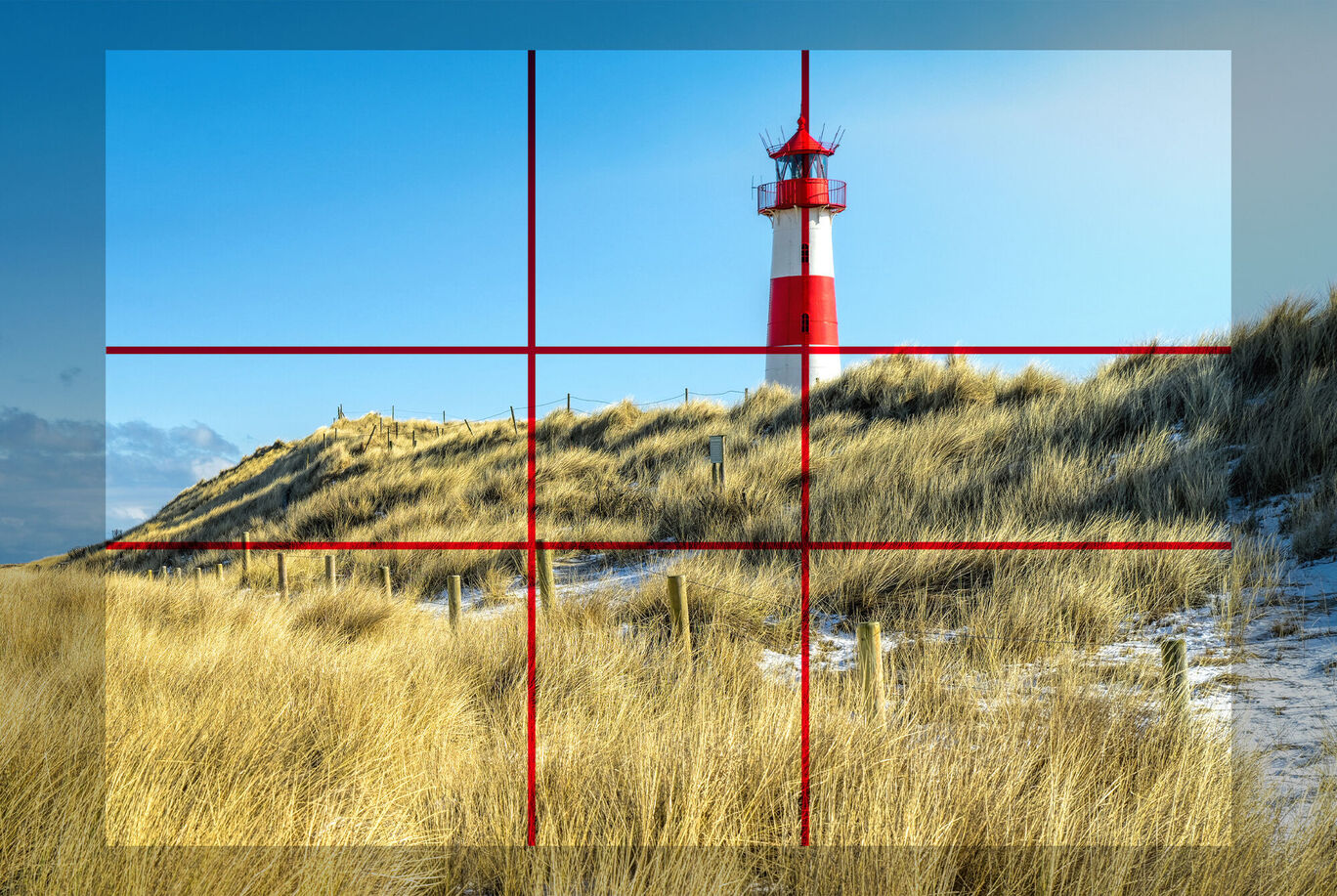 Faro su una duna di sabbia, circondato da erba alta e cielo pallido