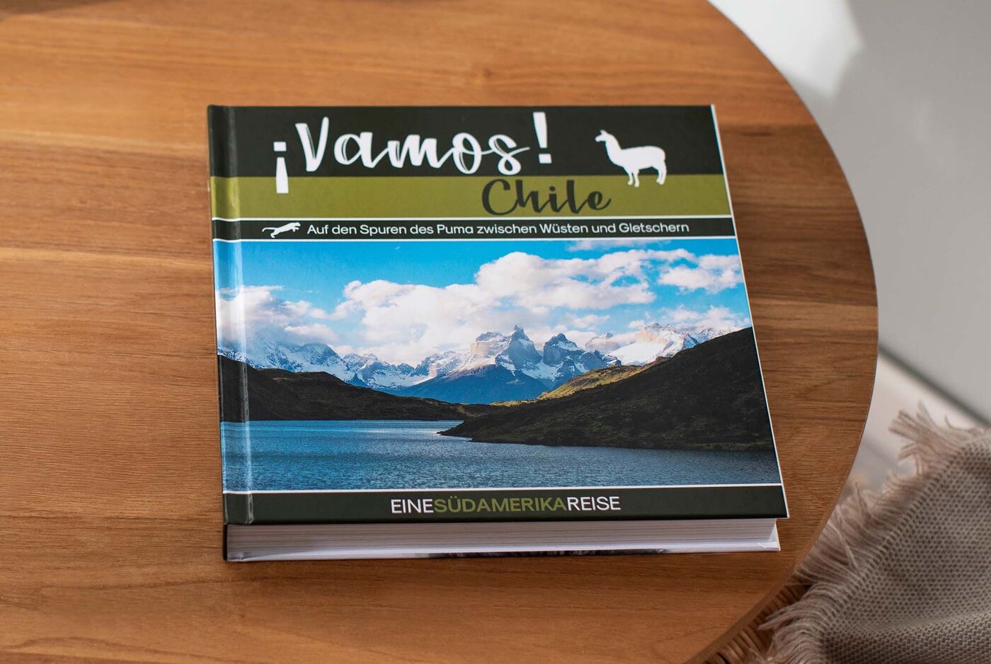 Un CEWE FOTOBUCH dal titolo ¡Vamos! Cile su un tavolo di legno. Il libro mostra immagini di montagne e laghi in Cile.