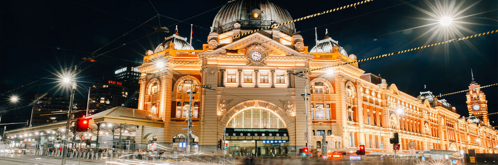 Bellamente illuminato, l'edificio storico della stazione di Flinders Street a Melbourne di notte, circondato da luci.