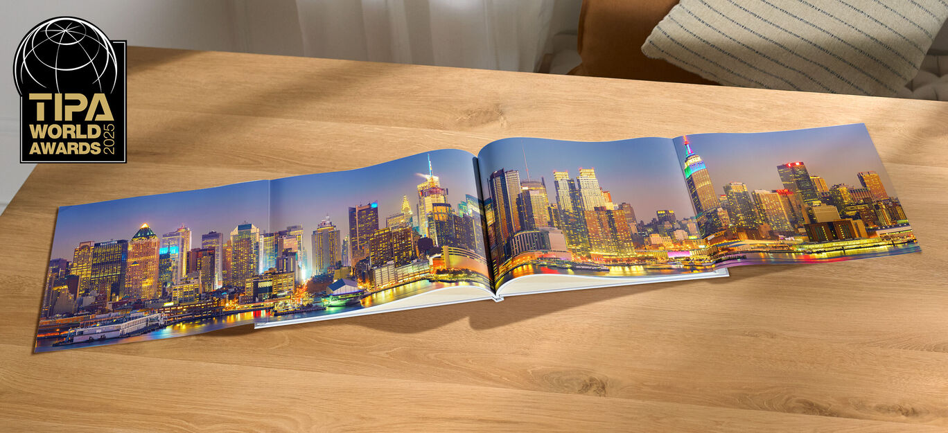 Un CEWE FOTOBUCH aperto su un tavolo di legno, con una panoramica di uno skyline illuminato di notte