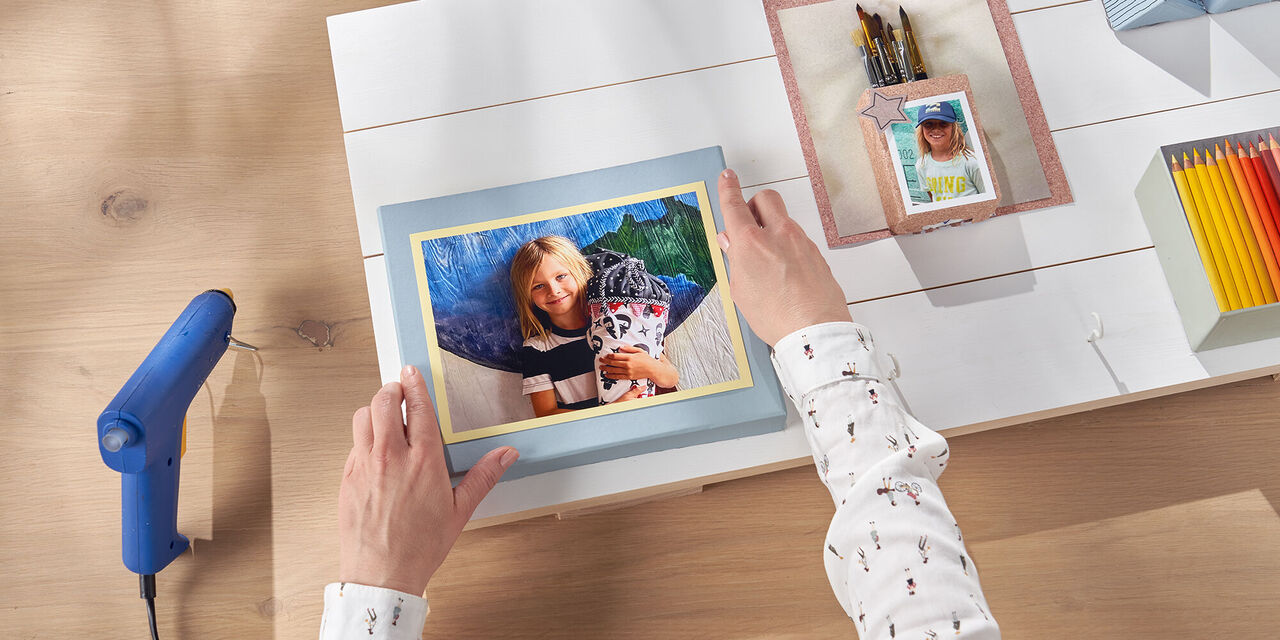 Una persona crea un album fotografico colorato su un tavolo con materiali creativi.