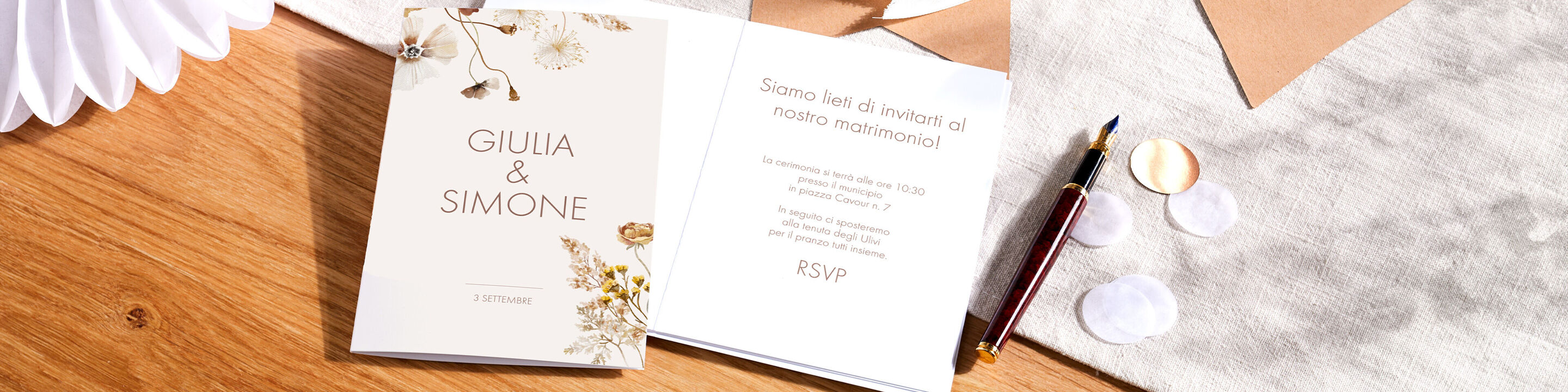 Biglietto d'invito in colori tenui con dettagli floreali, posato su un tavolo.